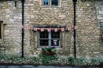 Rustic stone facade of a traditional British house with flag bunting and flowers.